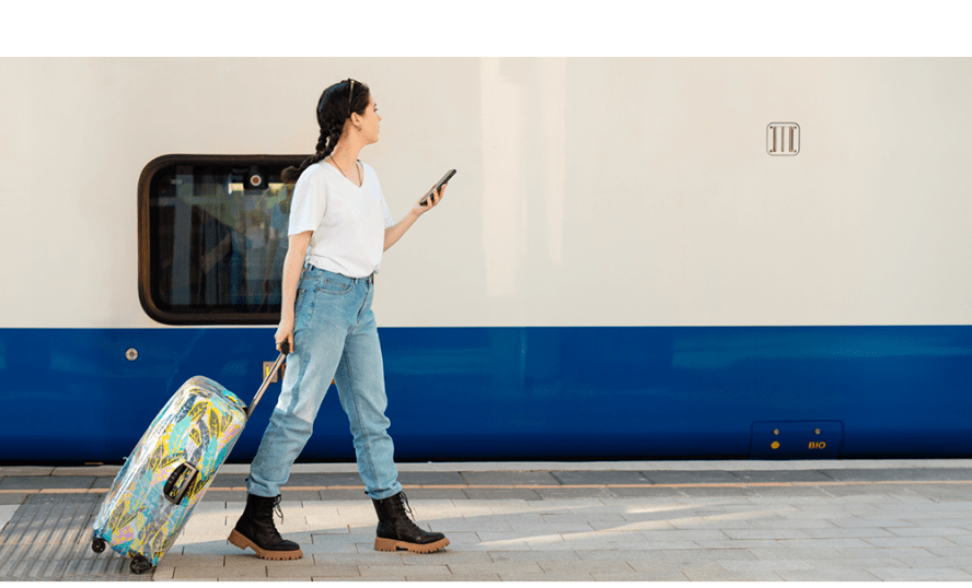 Ung kvinna som går av eller på ett tåg och kollar i sin telefon och drar sin resväska.